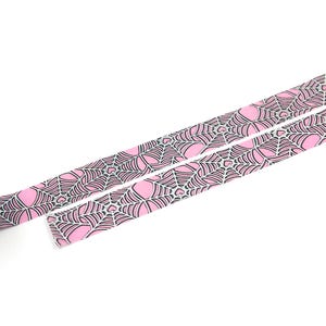 May include: A roll of pink and black washi tape with a spiderweb pattern. The tape is unrolled and shows the design.