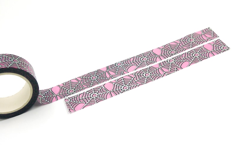 May include: A roll of pink and black washi tape with a spiderweb pattern. The tape is unrolled and shows the design.