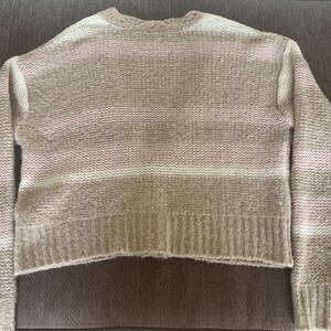 May include: A beige and white striped sweater with long sleeves. The sweater has a ribbed hem and cuffs. The stripes are horizontal and vary in width. The sweater is made of a soft, textured knit material.