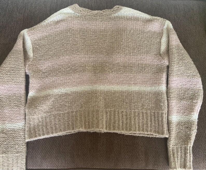 May include: A beige and white striped sweater with long sleeves. The sweater has a ribbed hem and cuffs. The stripes are horizontal and vary in width. The sweater is made of a soft, textured knit material.