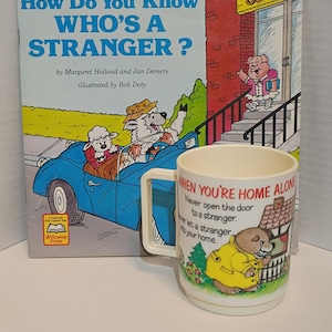 May include: A children's book titled "How Do You Know Who's a Stranger?" and a matching mug. The book cover features a blue car with animal characters. The mug has text that reads "When You're Home Alone".