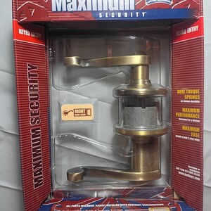 May include: A new Kwikset Maximum Security door handle set in its original packaging. The handle is a brass color with a lever design. The packaging is red, blue, and white, with the words "Maximum Security" prominently displayed.