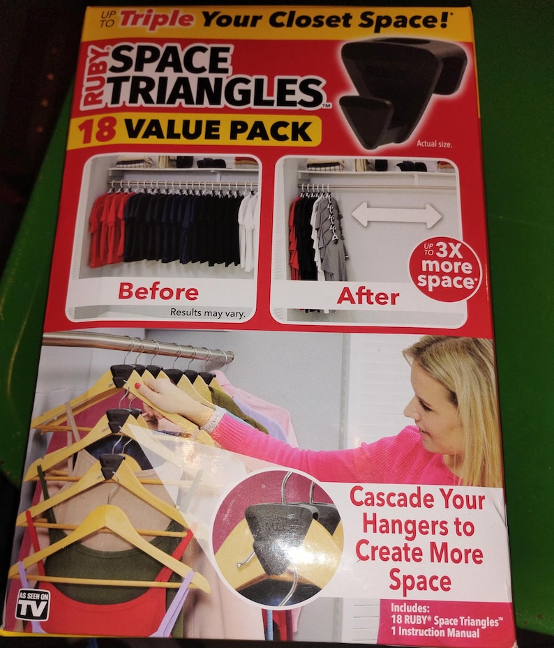 Op de afbeelding: Een rode en gele doos voor "RUBY Space Triangles" met de tekst "Triple Your Closet Space!" en "18 VALUE PACK". De doos toont voor- en na-vergelijkingen van de kastruimte. Inclusief 18 Space Triangles en een handleiding.