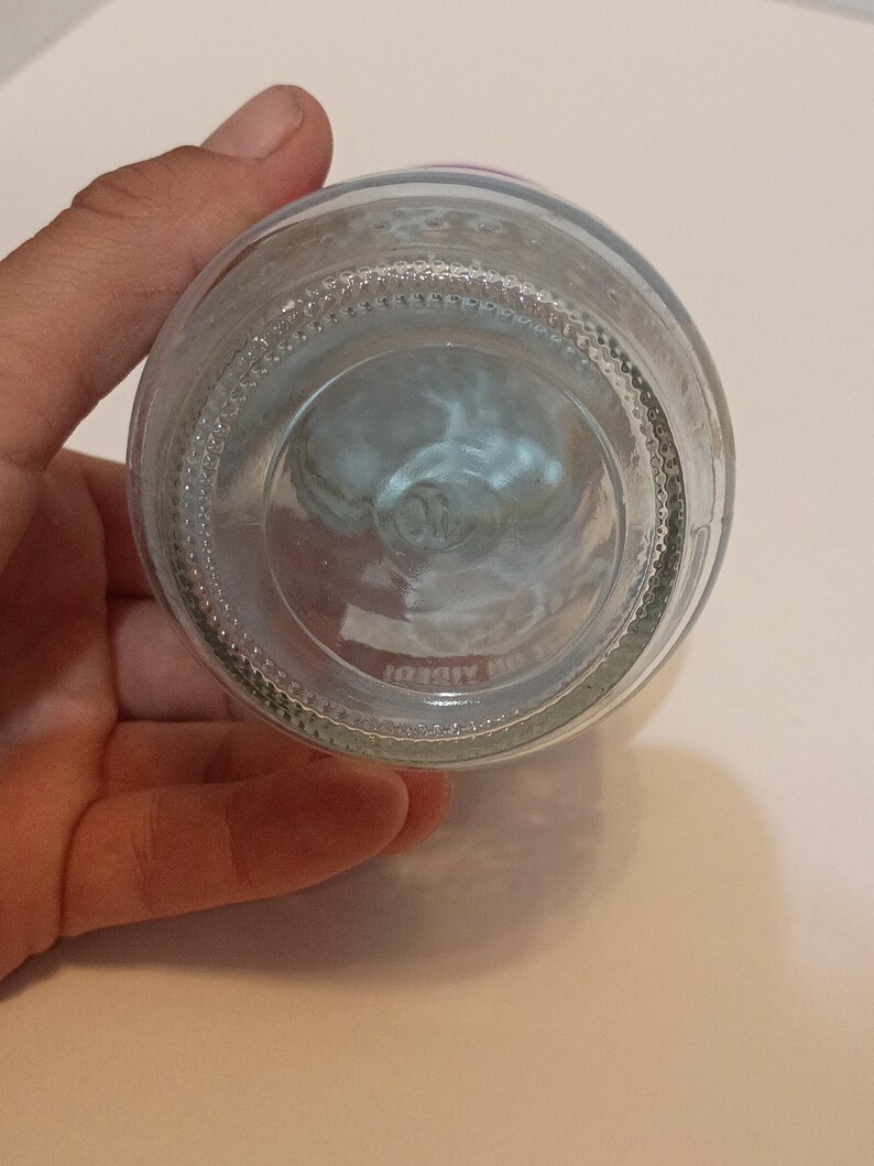 Puede incluir: Botella de vidrio transparente con base texturizada y forma redondeada. La botella es sostenida por una mano, mostrando su transparencia. La base tiene un dise&ntilde;o circular.