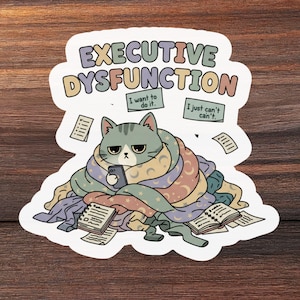 May include: A sticker depicting a grey cat with a phone, surrounded by blankets and papers. The sticker reads "EXECUTIVE DYSFUNCTION" with the phrases "I want to do it" and "I just can't can't."