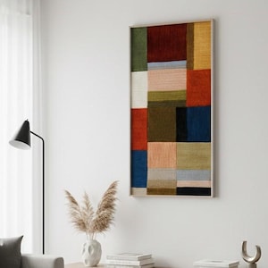 May include: A framed abstract wall art piece with a geometric design. The artwork features a patchwork of colorful rectangular shapes in shades of red, blue, green, and yellow. The frame is a light wood color.