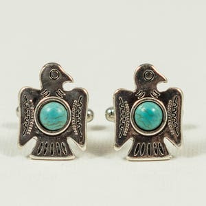 May include: A pair of silver cufflinks with turquoise stones in the centre. Each cufflink features a stylised bird design.