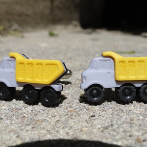 May include: A pair of cufflinks shaped like miniature dump trucks. The trucks are gray with yellow dump beds and black wheels.