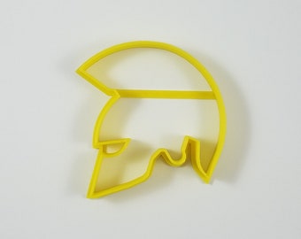 Könnte beinhalten: Ein hellgelber Ausstecher in Form eines spartanischen Helms. Der Ausstecher ist aus Kunststoff gefertigt und hat ein schlichtes, klares Design. Die Helmform ist eine klassische Darstellung antiker griechischer Krieger.