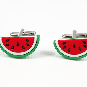 May include: A pair of watermelon cufflinks. The cufflinks are made of metal and feature a green, white and red watermelon design.