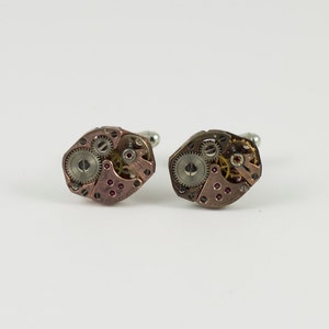 May include: A pair of cufflinks made from antique watch parts. The cufflinks are silver and gold in color and have a detailed design.
