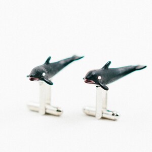 Op de afbeelding: Een paar zilveren manchetknopen met zwarte orka-walvisfiguren. De walvissen bevinden zich in zwempositie met witte markeringen op hun lichaam.
