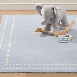May include: A pale blue rectangular rug with a cream dotted border. A grey plush elephant rocking toy with wooden rockers sits on the rug. Two small books are stacked near the elephant.