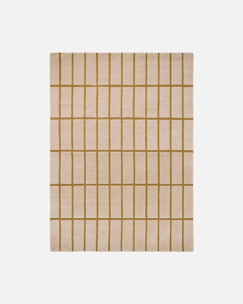 May include: A rectangular rug with a grid pattern. The rug has a light beige background with a series of vertical and horizontal lines in a mustard yellow color, creating a geometric design. The rug is made of a soft, plush material.
