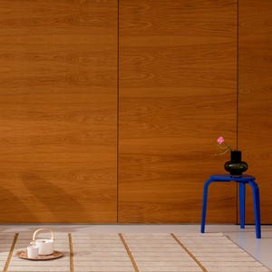 May include: A room scene featuring a light beige rug with brown stripes, a small blue table holding a black vase with a pink flower, and a wooden cabinet. A tea set sits on a wooden tray on the floor.