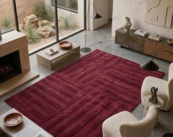 May include: A large rectangular area rug in a deep burgundy red color featuring a textured pattern of raised horizontal and vertical lines that create a grid-like design across the surface, covering the floor in a living room space.