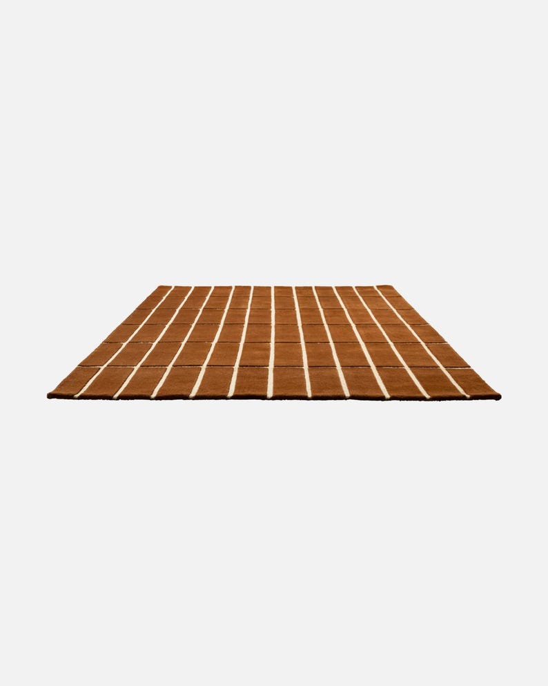 May include: A rectangular brown rug with vertical white stripes. The rug has a textured appearance and is placed on a white background. The rug is a home decor item, suitable for living rooms or bedrooms.