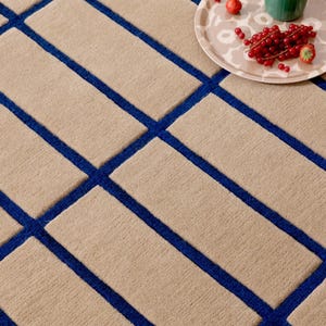 May include: Beige rectangular rug with a geometric pattern of blue lines. The rug has a textured surface. A tray with strawberries and red currants sits on the rug.