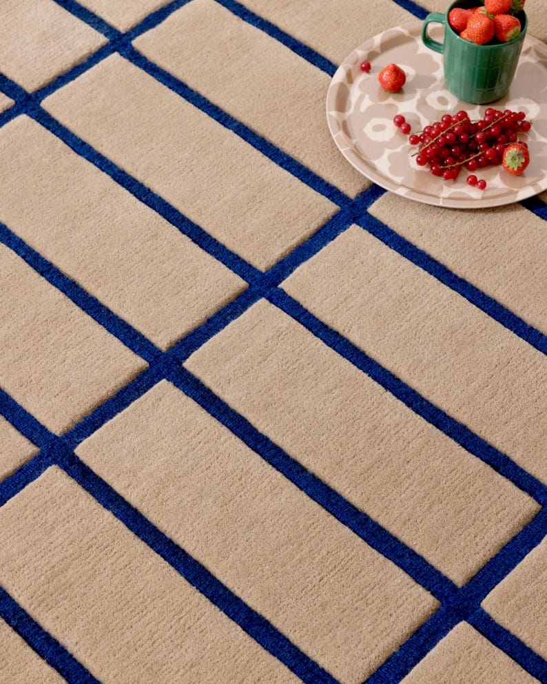 May include: Beige rectangular rug with a geometric pattern of blue lines. The rug has a textured surface. A tray with strawberries and red currants sits on the rug.