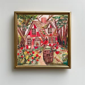 Könnte beinhalten: Gerahmtes Gemälde eines malerischen Cottage mit rotem Dach und weißen Wänden, umgeben von üppigem Grün und roten Rosen. Ein Kardinal sitzt auf einem Korb, ein weiterer Vogel steht in der Nähe. Das Kunstwerk hat eine warme, einladende Ausstrahlung.