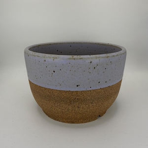 May include: A set of three ceramic mugs with a speckled, matte finish. The mugs are in shades of cream, light gray, and dark gray. Each mug has a simple, minimalist design and a rounded handle.