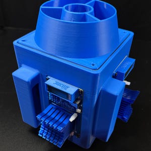 Puede incluir: Un dispositivo electrónico azul, impreso en 3D, con una base cuadrada y una parte superior en forma de embudo. El dispositivo tiene múltiples aletas de refrigeración y pequeñas placas de circuito con el texto "JACQUES" y "EdiTune".