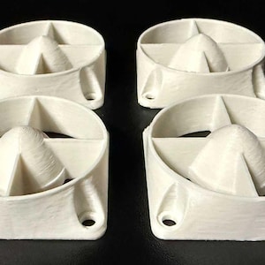 May include: Four off-white, circular objects with a central, rounded triangular shape and a surrounding ring. Each object has two holes on the base. The objects are arranged on a black surface.
