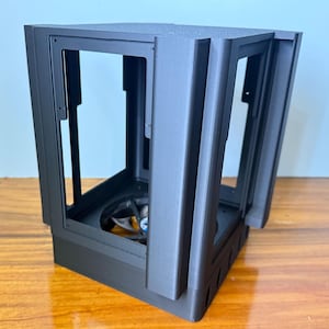 Peut inclure: Un boîtier d'ordinateur noir avec une conception à cadre ouvert. Le boîtier a une forme rectangulaire avec un dessus et des panneaux latéraux texturés. L'intérieur révèle un ventilateur et d'autres composants.