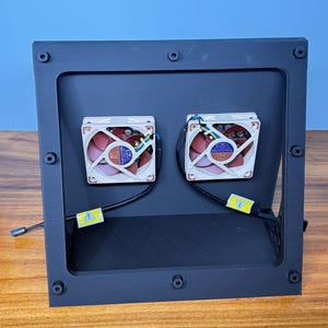 Peut inclure: Un cadre rectangulaire noir avec deux ventilateurs carrés. Les ventilateurs ont des cadres blancs, des pales rouges et des autocollants bleus et dorés. Le cadre a plusieurs vis et est sur une surface en bois avec un fond bleu.