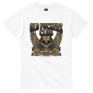 May include: A white short-sleeved t-shirt featuring a graphic of a skull with wings and an eye on its forehead. The text reads OLD FUCKERS CLUB, LIFETIME MEMBER, 100% BITTER, and LOADED AND PROUD. The design uses shades of brown, black, and tan.