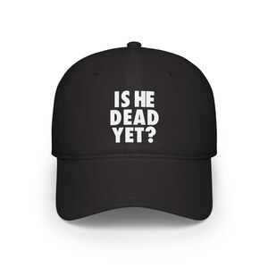 May include: Black baseball cap featuring the white text "IS HE DEAD YET?" on the front. The cap has a curved peak and a structured crown. A classic style of hat, suitable for casual wear.