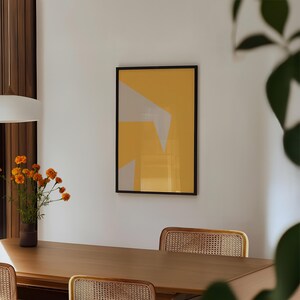 May include: A rectangular wall art piece in a thin black frame featuring a mustard yellow background with two light gray geometric shapes. The top shape is a large triangle pointing downward, and the bottom shape is a smaller irregular polygon.