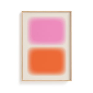 May include: Abstract art print featuring two blurred rectangular shapes, one pink and one orange, set against a cream background. The artwork is framed in a light wood frame, creating a modern and minimalist aesthetic.