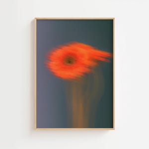 Puede incluir: Una impresión artística enmarcada con una imagen borrosa de una flor naranja brillante sobre un fondo gris azulado oscuro. El centro de la flor es de un naranja más oscuro, con un toque de amarillo. Tema floral abstracto.