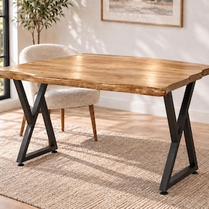 May include: A rectangular dining table featuring a natural light brown wood grain top with an uneven live edge finish. The table is supported by two black metal legs, each constructed with a geometric X-shaped frame design that provides stability.