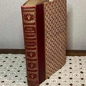 May include: A vintage hardcover book titled "Tales from the Decameron" by Boccaccio. The spine is burgundy with gold lettering and decorative elements. The cover features a patterned design in beige and burgundy, with a "Collector's Edition" label.