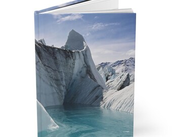 May include: Hardcover journal featuring a scenic photograph of a glacier and turquoise water. The cover image shows a large, icy formation under a blue sky with wispy clouds. The journal is open, revealing the white pages inside.