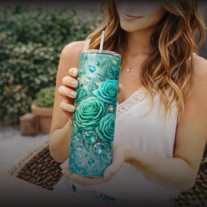 May include: A teal and turquoise tumbler with a floral rose design. The stainless steel tumbler features large teal roses, sparkling gems, and a silver straw. The design is set against a glittery background, creating a decorative drinkware item.
