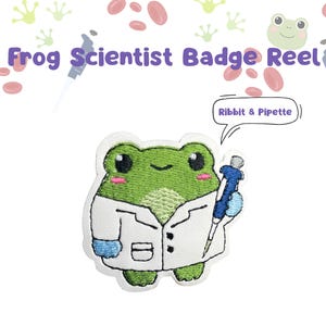 May include: An embroidered badge reel featuring a green frog wearing a white lab coat and holding a blue pipette. A speech bubble above the frog contains the text Ribbit & Pipette. The words Frog Scientist Badge Reel appear at the top.