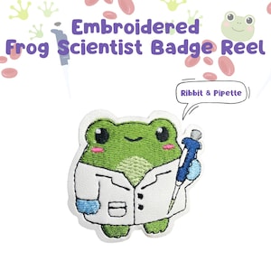 May include: An embroidered badge reel featuring a green frog wearing a white lab coat and blue gloves, holding a blue pipette. A speech bubble above the frog contains the text Ribbit & Pipette. The background includes frog and blood cell graphics.