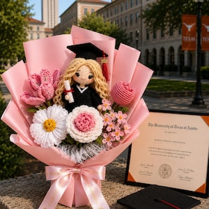 Puede incluir: Una muñeca de ganchillo con birrete y toga de graduación negra, sosteniendo un diploma, en un ramo de flores de ganchillo rosas, blancas y amarillas, envuelto en papel rosa con una cinta que dice Congratulations, junto a un diploma y birrete.