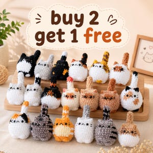 May include: A collection of small, round, crocheted cat figurines in various colors and patterns, including solid, striped, and spotted designs. Each cat features a vertical tail and black bead eyes. The text "buy 2 get 1 free" is displayed above.