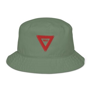 May include: A green bucket hat with a red triangle embroidered on the front. The triangle has the word "YIELD" written inside.