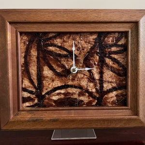 May include: A wooden framed clock with a brown and black patterned face. The clock is on a white stand.
