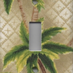 May include: A light brown switch plate with a tropical palm tree pattern. The plate has a white rectangular cutout for a light switch.