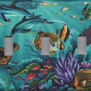 May include: A turquoise blue light switch cover with a colorful underwater scene. The scene features two dolphins, a sea turtle, coral, and various fish.
