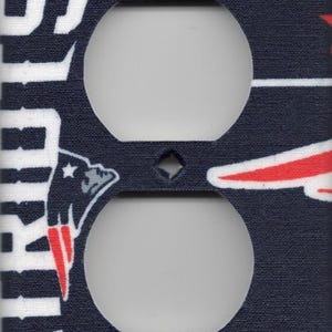 May include: A navy blue and white electrical outlet cover featuring the words "PATRIOTS" and team logos. The cover has two openings for outlets and a red star design.