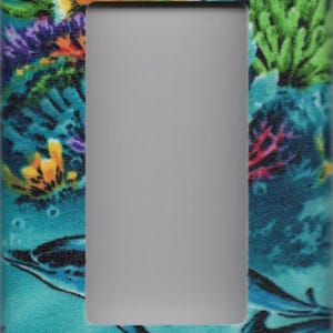 May include: A decorative light switch cover featuring a vibrant underwater scene. The design includes colorful coral, fish, and dolphins in shades of blue, green, yellow, and orange. The cover has a rectangular opening for the switch.