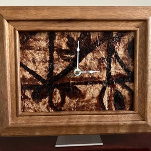 May include: A wooden framed clock with a brown and black patterned face. The clock has white hands and a gold center.