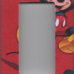 May include: Red light switch cover with a Mickey Mouse design. Mickey is wearing red shorts and yellow shoes. The switch cover has a white frame around the switch.